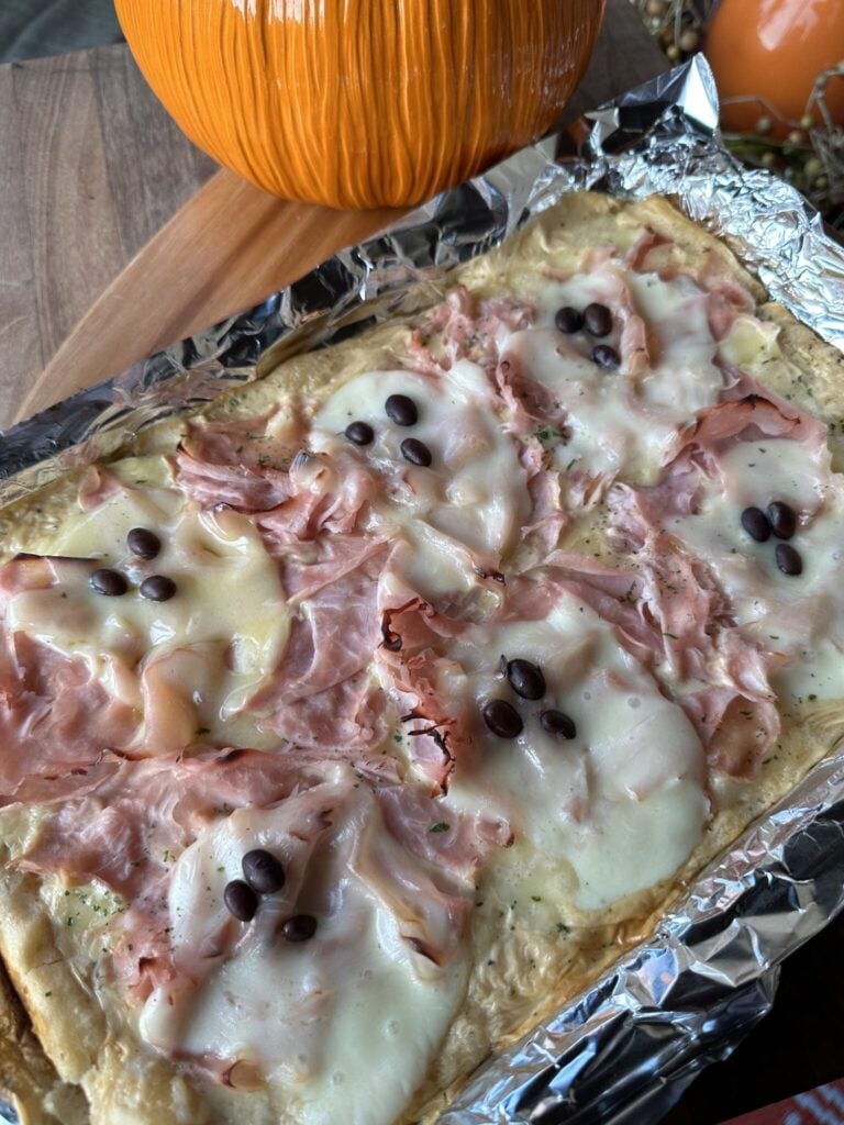 a tray of a pastry tart that has cheese shaped into ghosts and black beans for the ghost face