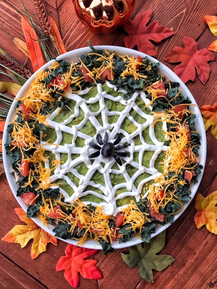 a taco dip made to look like a spiderweb with sour cream as the web