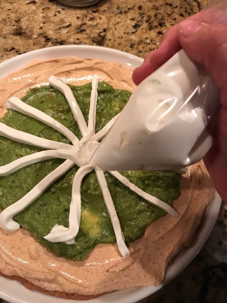 sour cream being used to draw the lines of a spiderweb with a piping bag