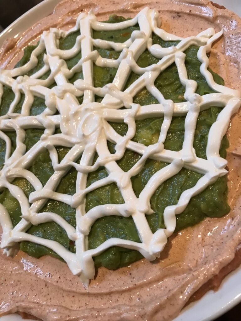  Sour cream being piped into a spider web on Halloween Taco Dip

