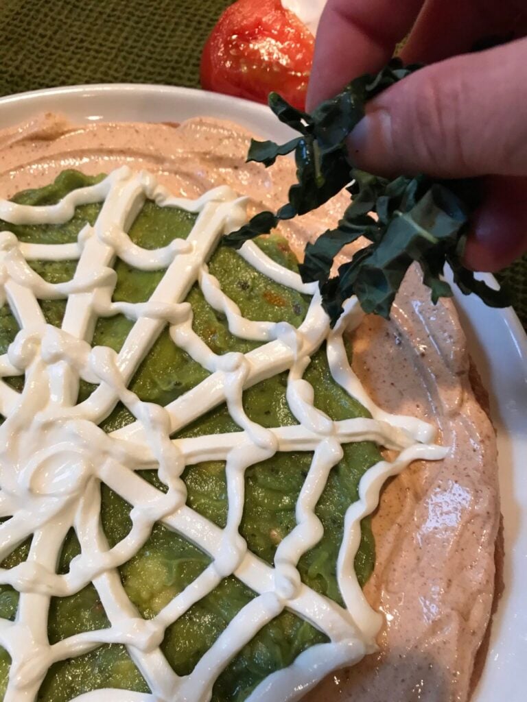 thinly sliced kale being added to the edges of the dip