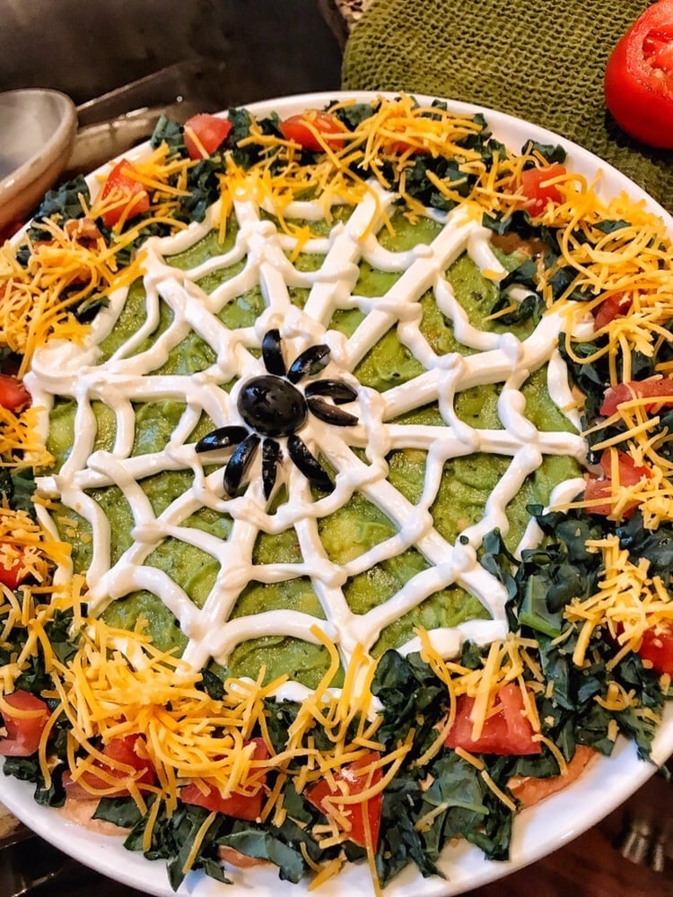 the finished taco dip with a sour cream spiderweb and the black olive spider