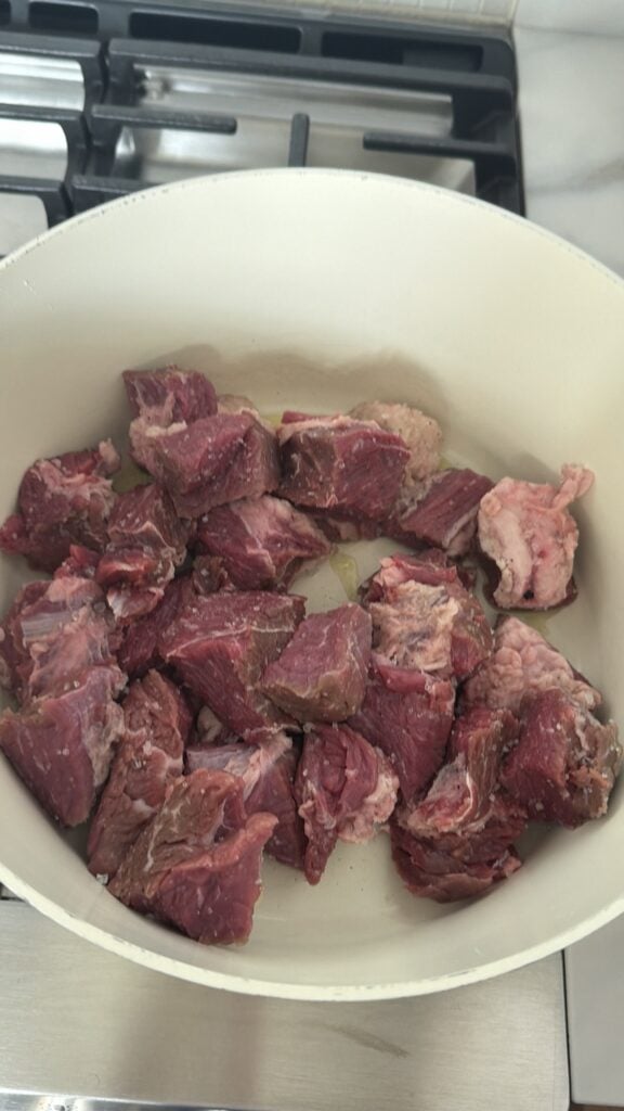 Pieces of chuck roast browning in a large pot before making spicy beef stew