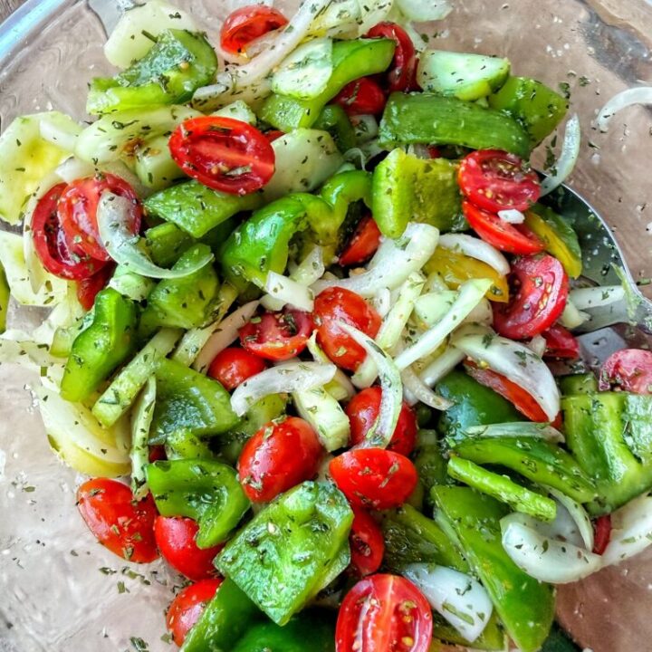 Green peppers, cucumber, tomatoes, and sliced sweet onion in a glass bowl with herb dressing.