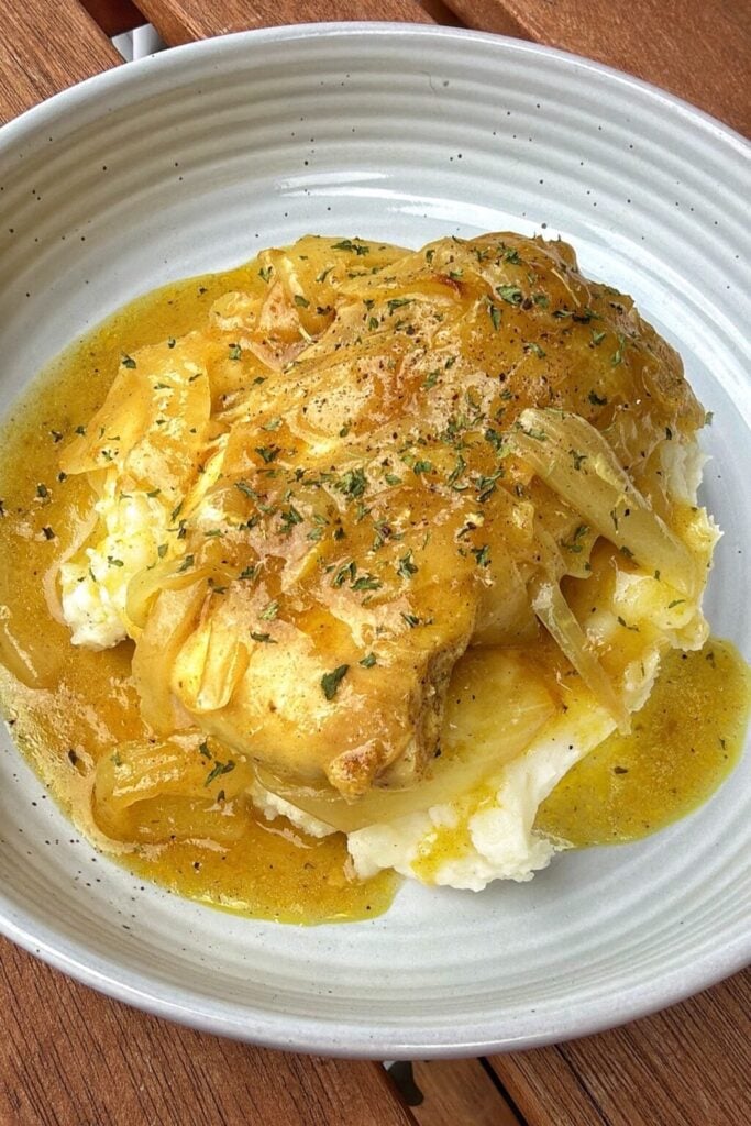 a plate of golden chicken and onions in gravy served over mashed potatoes