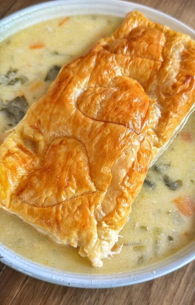 a bowl of chicken pot pie soup with a crispy puff pastry topper