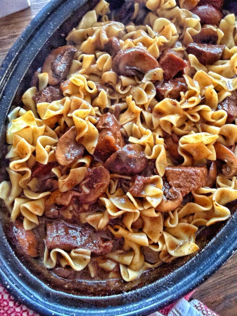 a roasting pan of beef chunks and noodles in a brown gravy