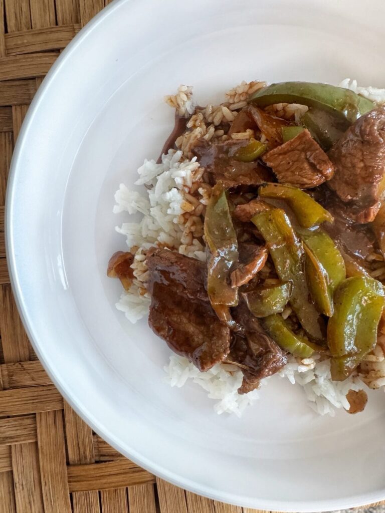 Skirt steak, peppers, onions and rice served on a white plate.