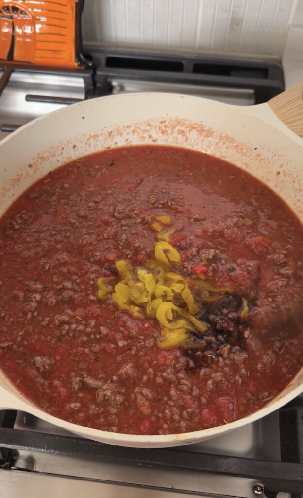 Browned ground beef cooking with giardiniera relish and pepperoncini peppers.