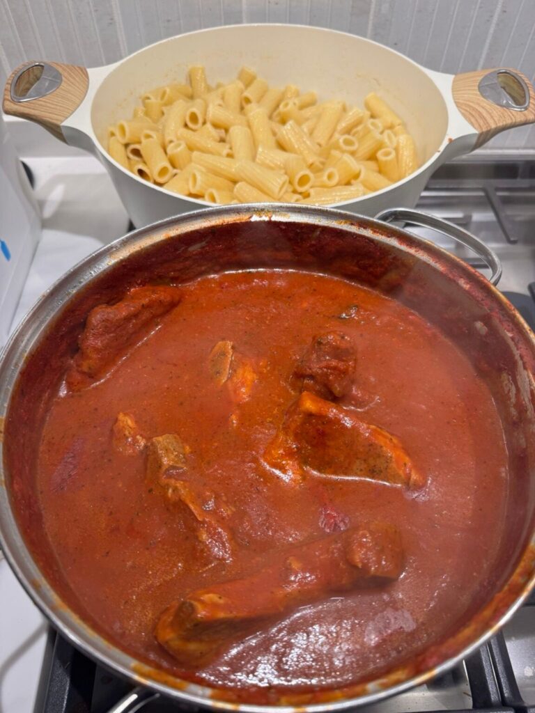 Pot of zesty sauce with pork chops and a pot of pasta