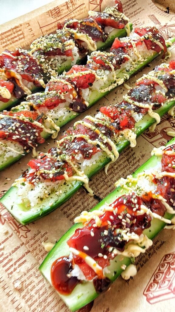 Sushi cucumber boats filled with rice and ahi tuna, drizzled with mayonnaise and sauce, and topped with furikake and jalapeños.
