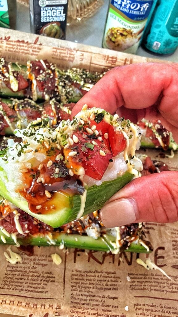 A cucumber half layered with seasoned sushi rice, thinly sliced tuna, and creamy sauce.