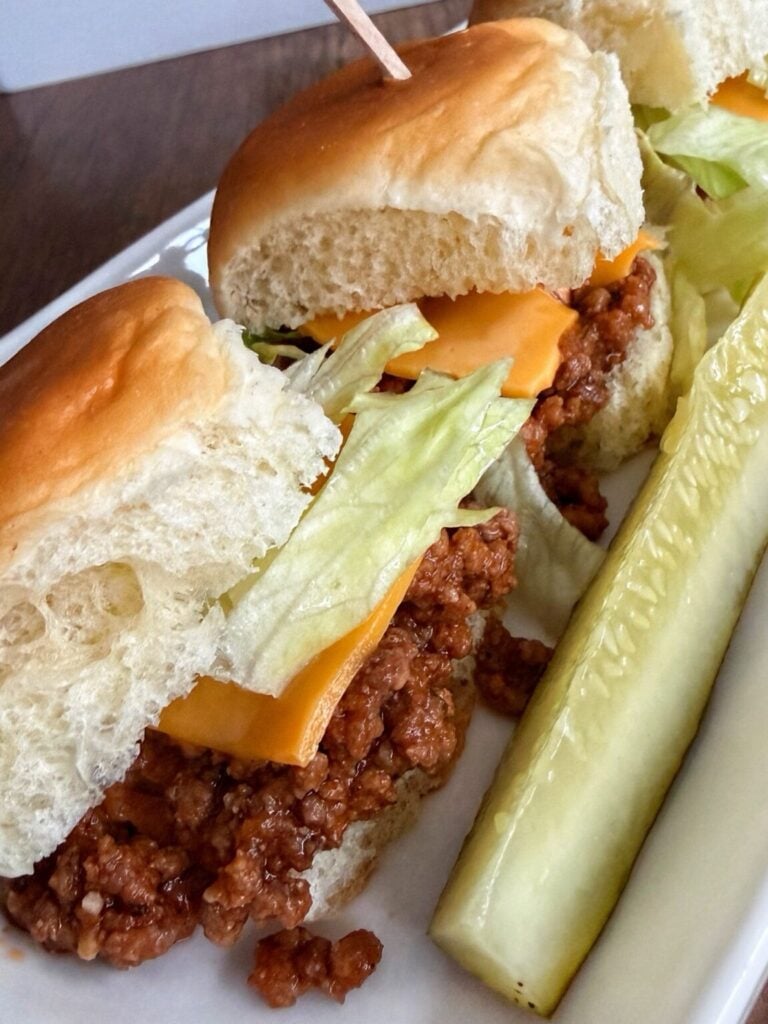 Two sloppy joe sliders with lettuce and cheese and served with a pickle