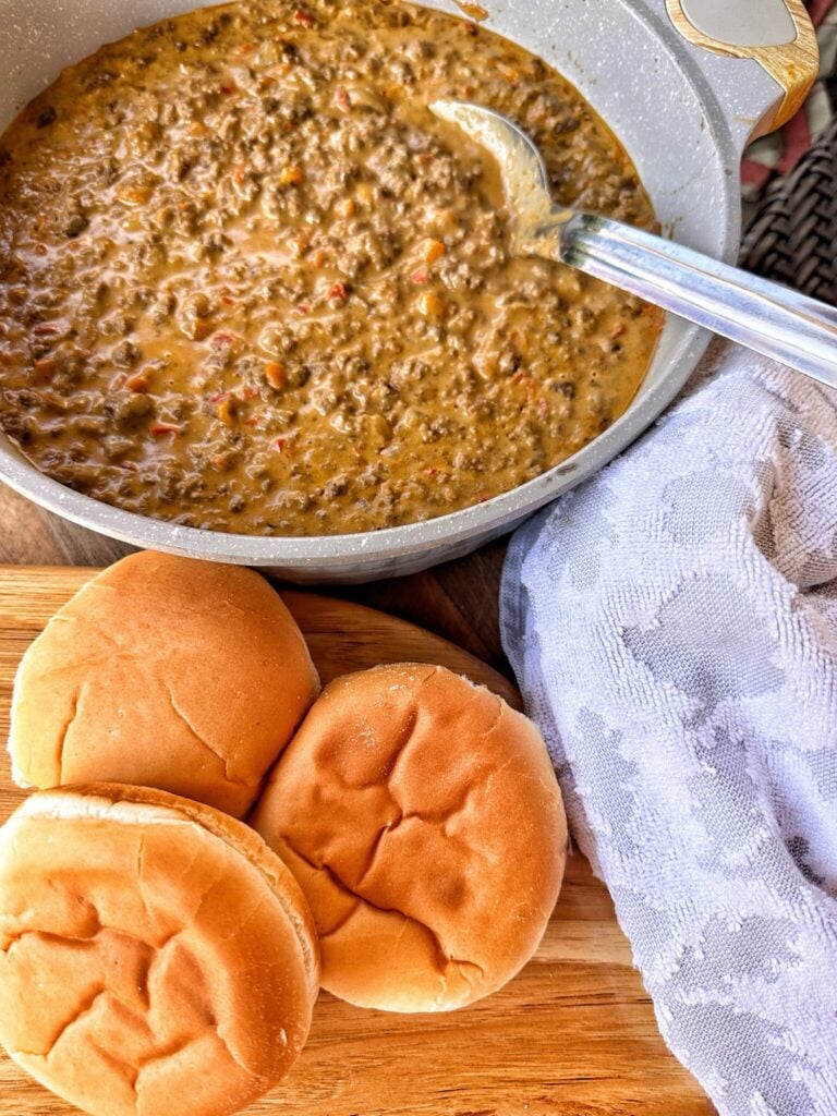 A pan of cheesy sloppy joe with buns on the side and a decorative towel