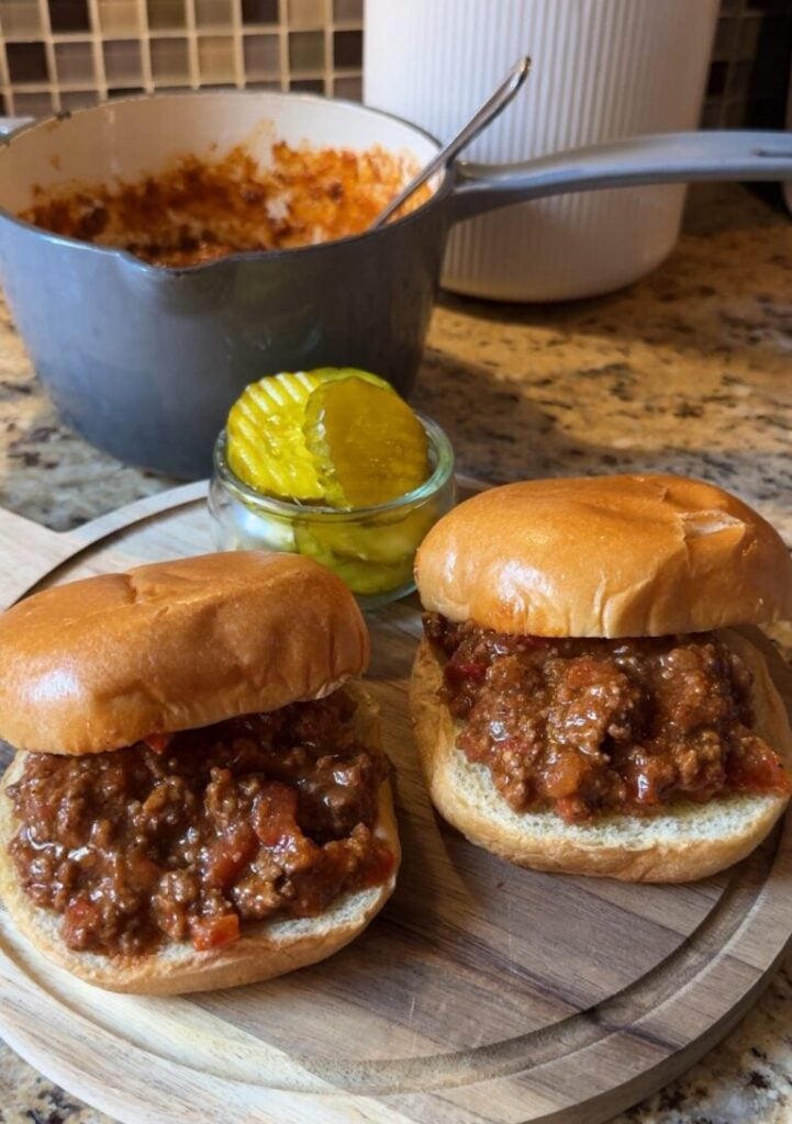 Barbecue beef sandwiches with crumbled beef on buns with a small bowl of pickles