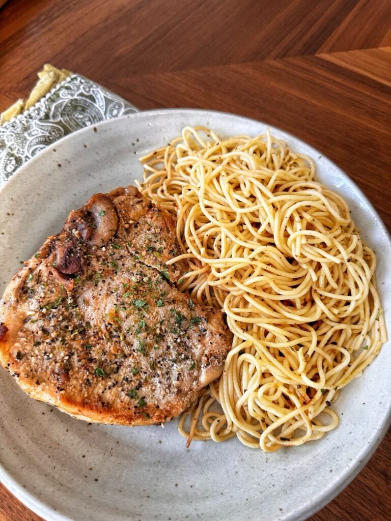 A supper club pork chop served alongside spaghetti