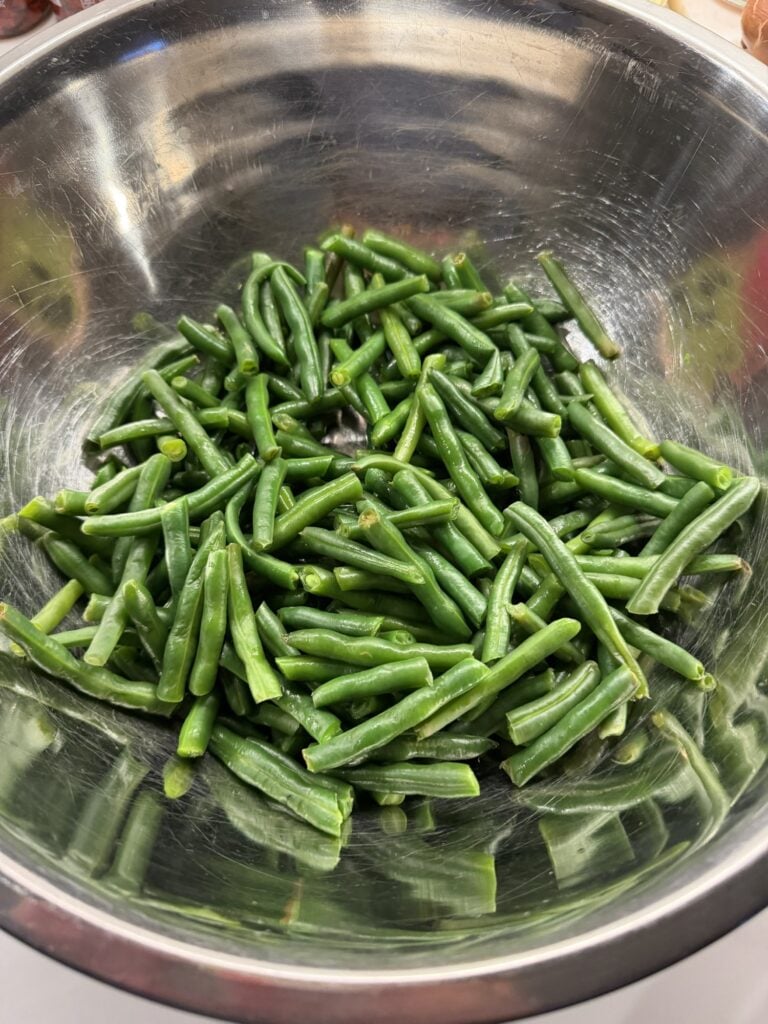 Blanched green beans cut into shorter pieces draining in a colander.