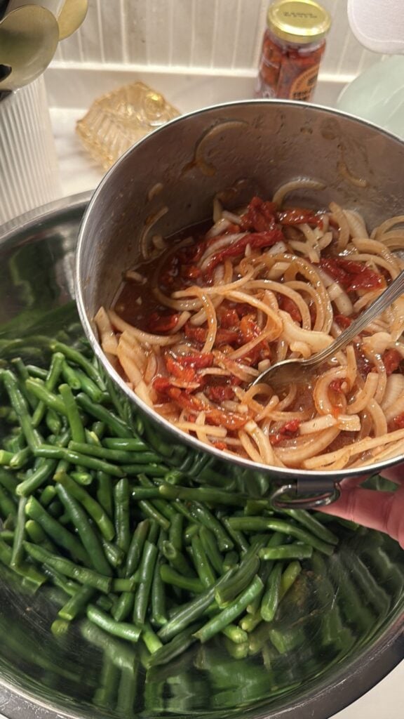 Green beans about to be mixed with sweet onions, sun-dried tomatoes, and Italian herbs in a bowl.