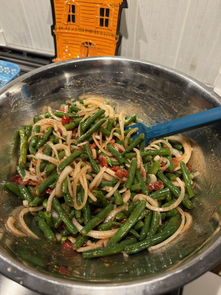 A serving of cold green bean salad with sweet onion and sun-dried tomatoes.