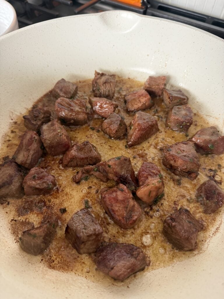Sirloin steak bites searing in a skillet with space between the pieces.