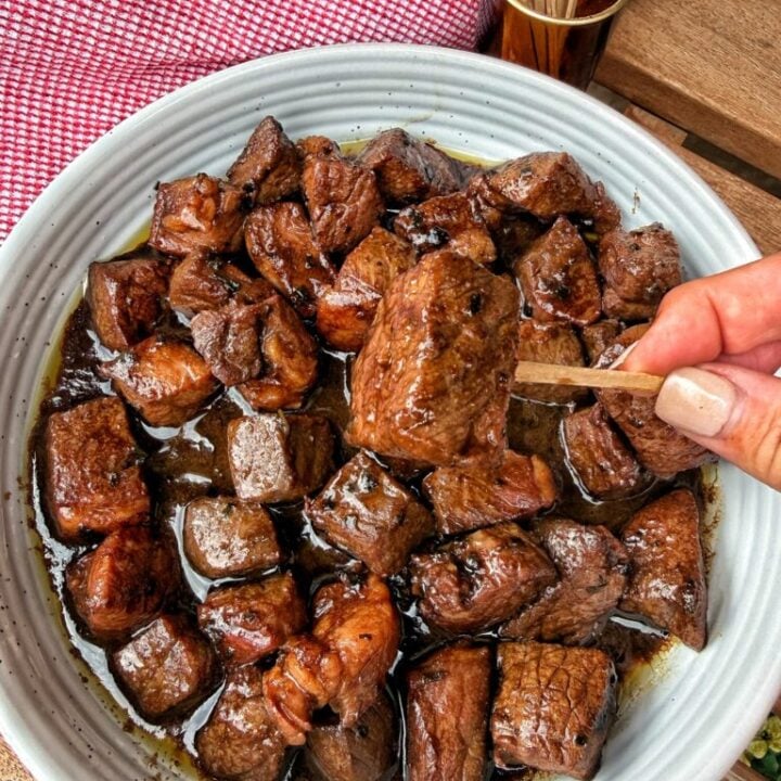 Sirloin steak bites in a bowl with one being held up with a tooth pick