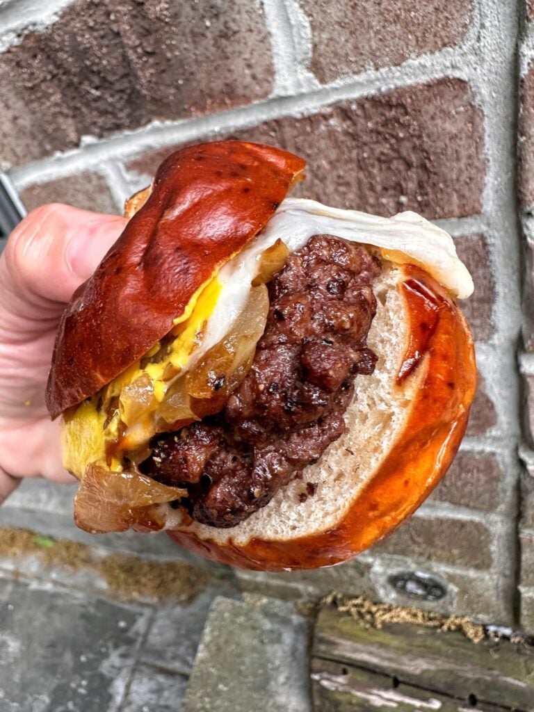 A mini burger on a pretzel slider roll with melted cheese