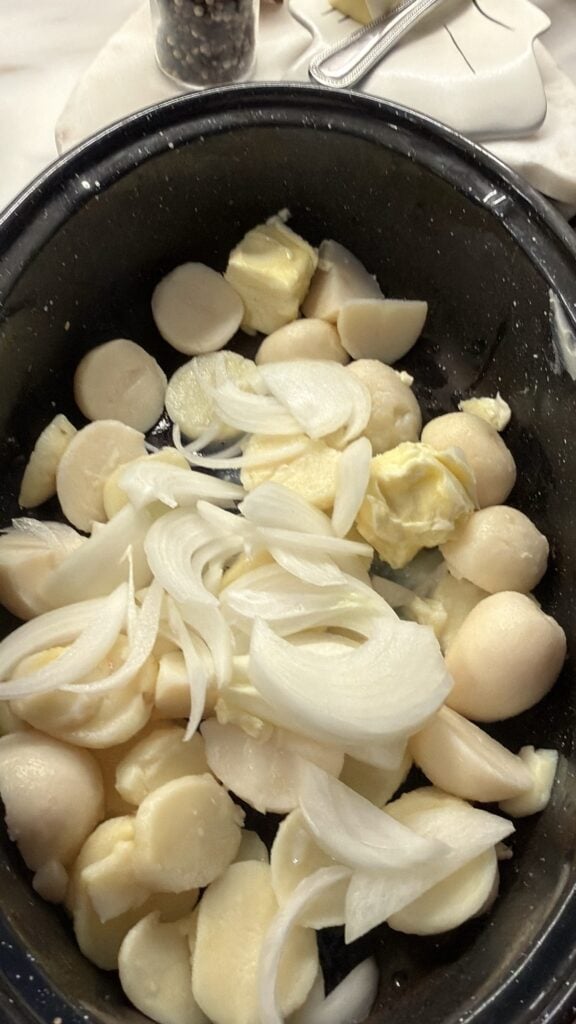 Drained canned potatoes ready to bake with ham and onions. pictured in the roaster with sliced onions