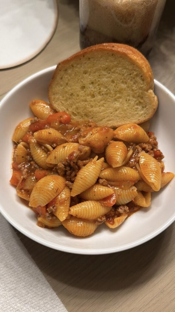 A serving of shell pasta coated in ground beef marinara sauce with diced peppers.