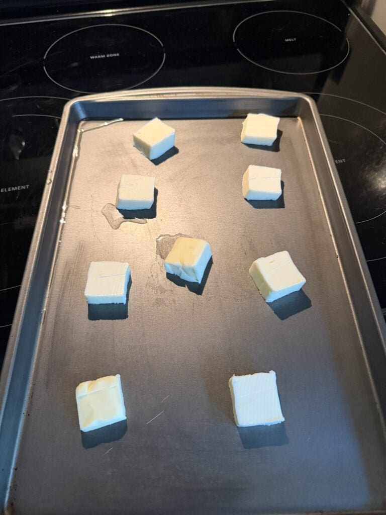Pieces of butter arranged on a rimmed baking sheet before melting in the oven.