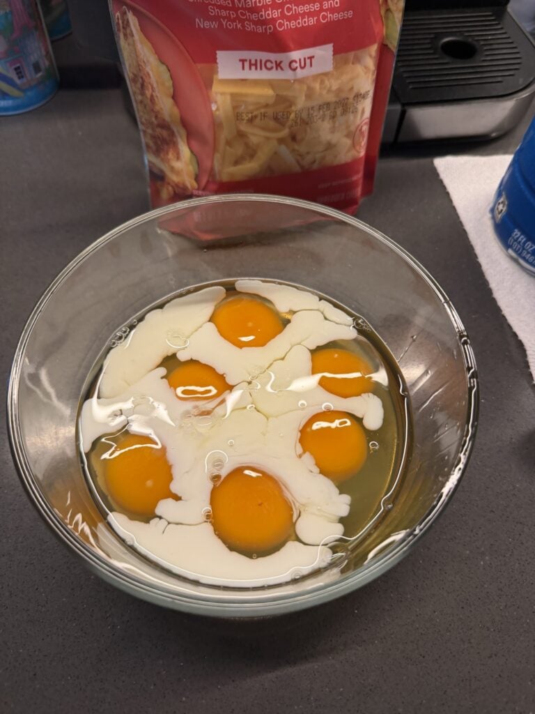 Bowl of whisked seasoned eggs beside a sheet pan of browned hash browns.