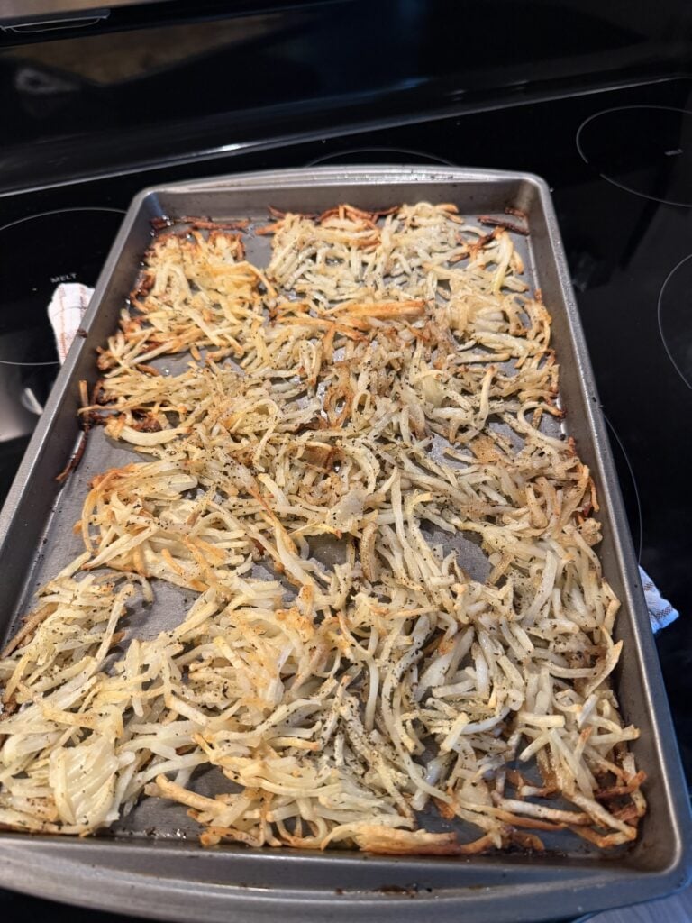 Shredded hash browns with golden brown edges after baking on a sheet pan.