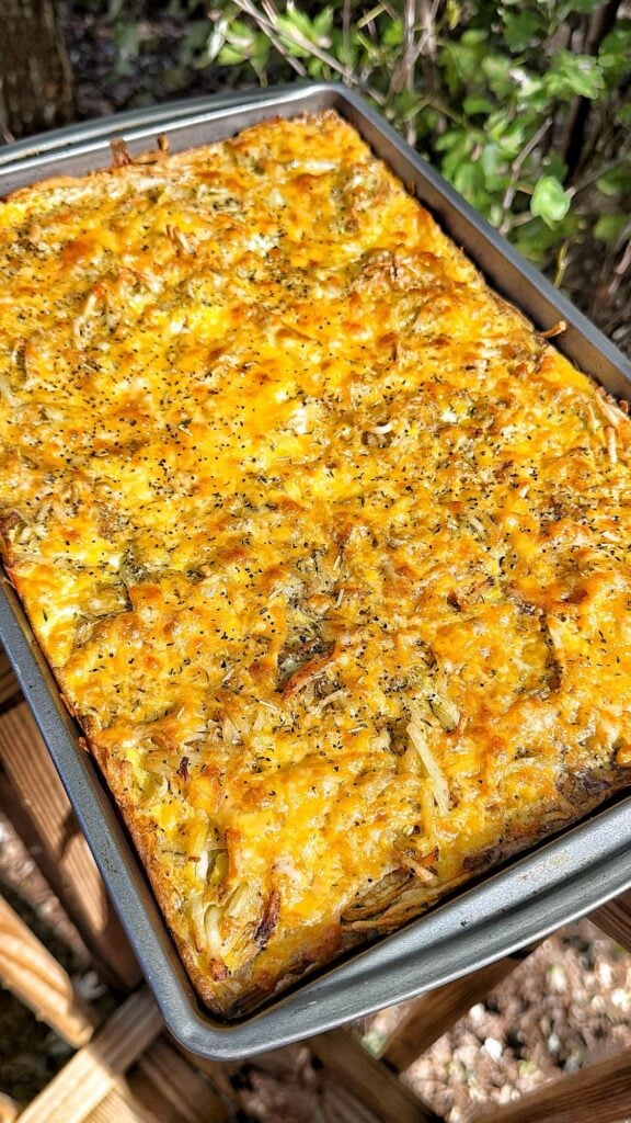 Golden cheddar cheese covering a sheet pan hash brown and egg bake.