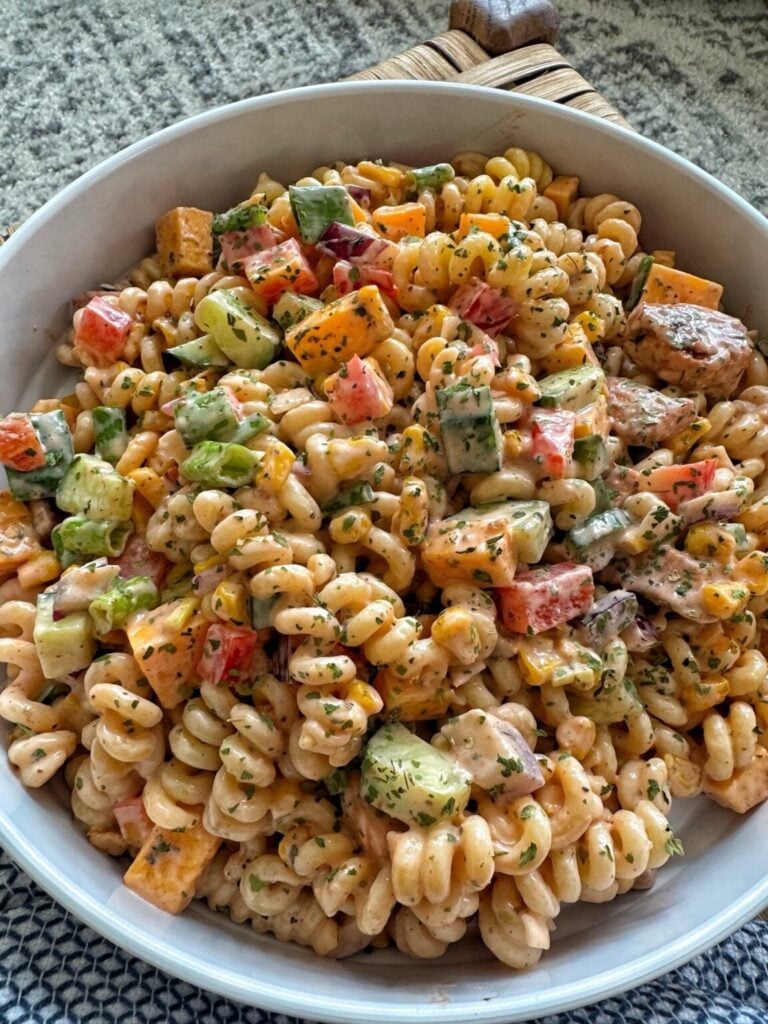 A bowl of barbecue chicken pasta salad with tri color noodles and dressing.