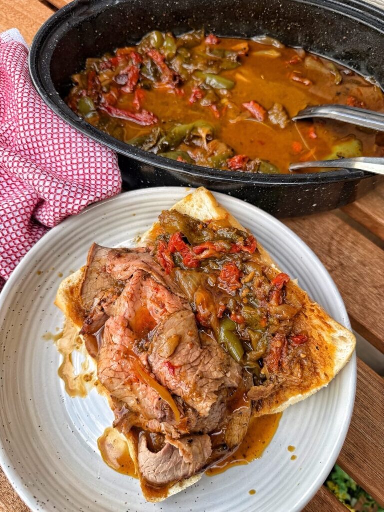 an Italian beef sandwich on bread with a pan of the beef and gravy on the side