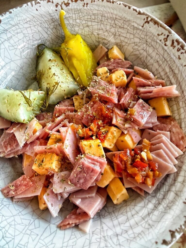 a bowl of chopped cold cuts and cheese with pickles and herbs