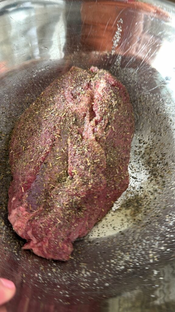 The uncooked sirloin tip roast in the roasting pan shown with the seasonings