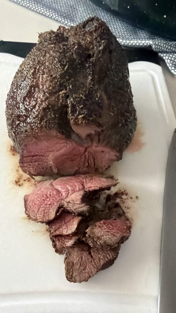 Sirloin tip roast carved into thin slices with a browned herb crust and pink center.