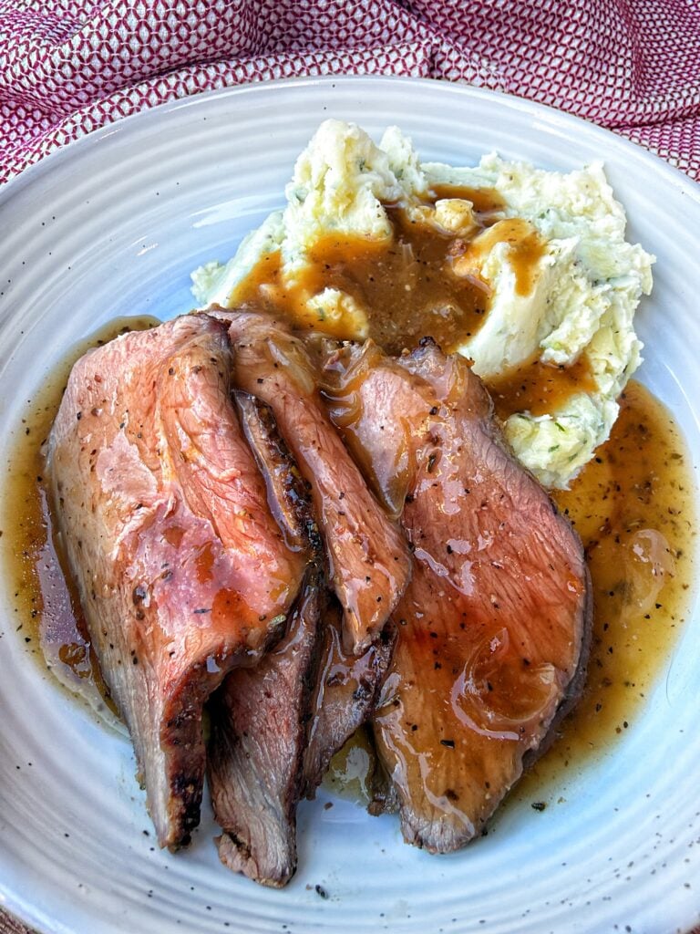Sliced roast beef beside creamy chive potatoes with onion gravy spooned over both.
