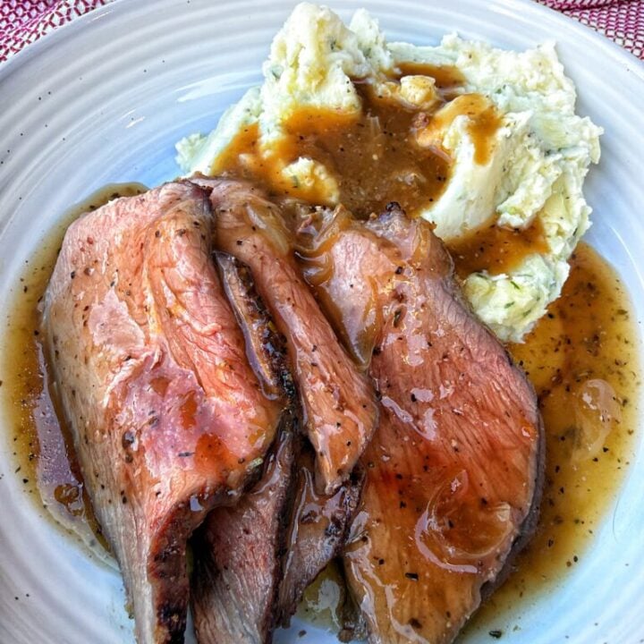 Sliced roast beef beside creamy chive potatoes with onion gravy spooned over both.