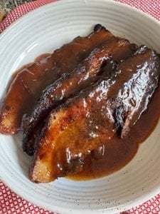 A gray plate with three slices of beef brisket with gravy on it