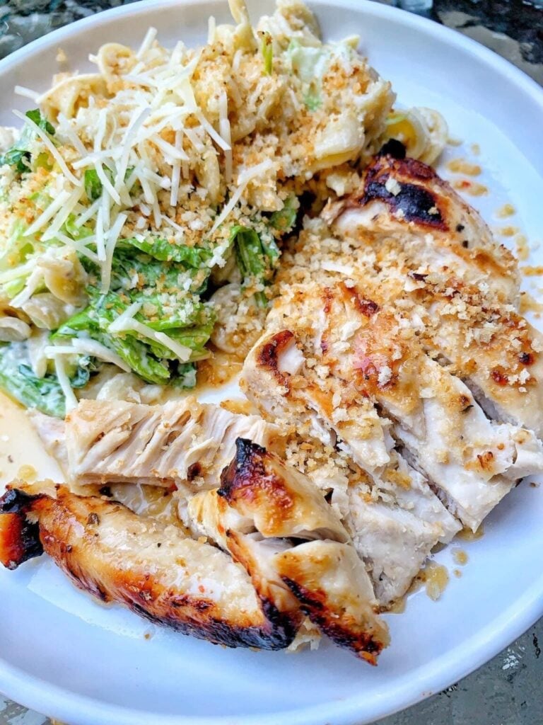 A plate with a chicken caesar pasta salad with a side of grilled chicken.