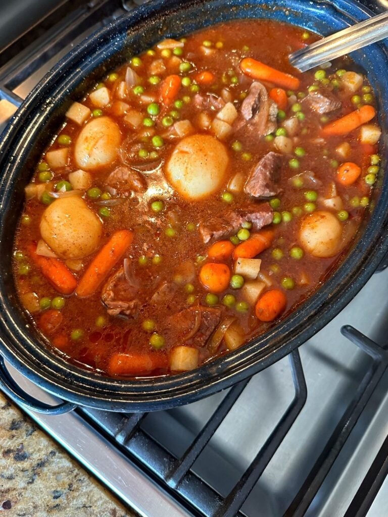a roasting pan with classic beef stew in it with beef, carrots, onions, peas and potatoes in a brown gravy