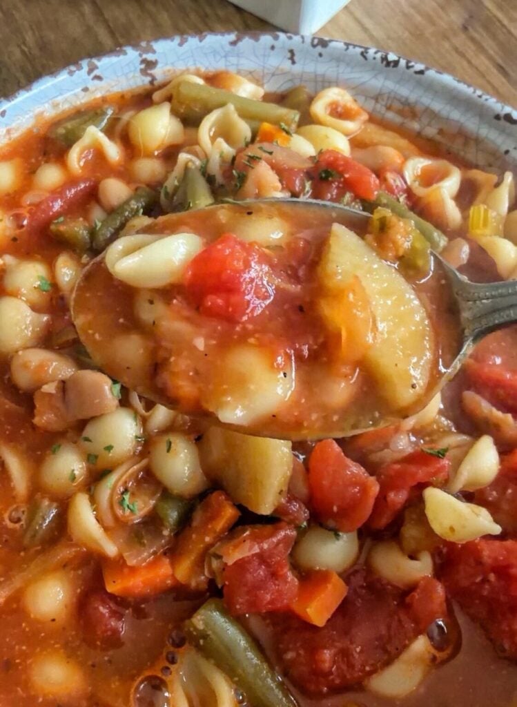 a bowl of minestrone soup with a spoonful of the soup lifted out of the bowl