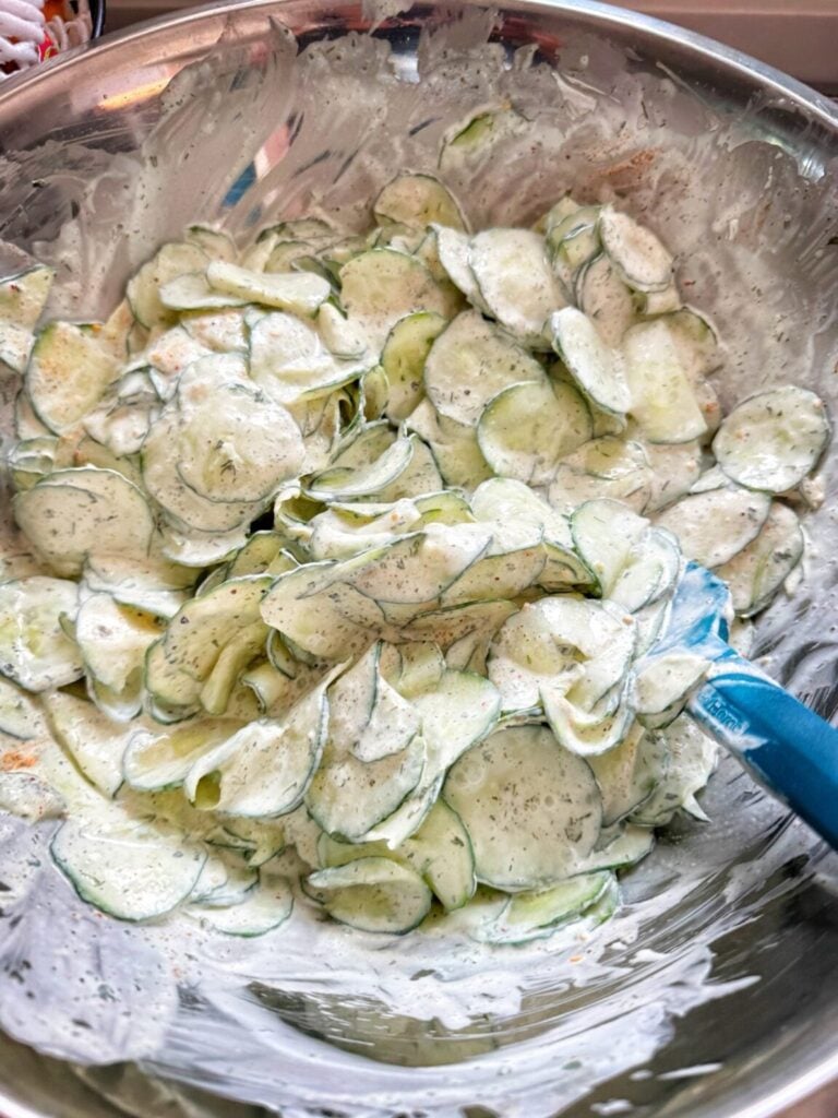 thin slices of cucumber in a large bowl with a creamy dressing