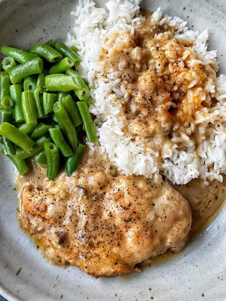 A piece of Swiss chicken with rice, both have gravy and then a side of green beans