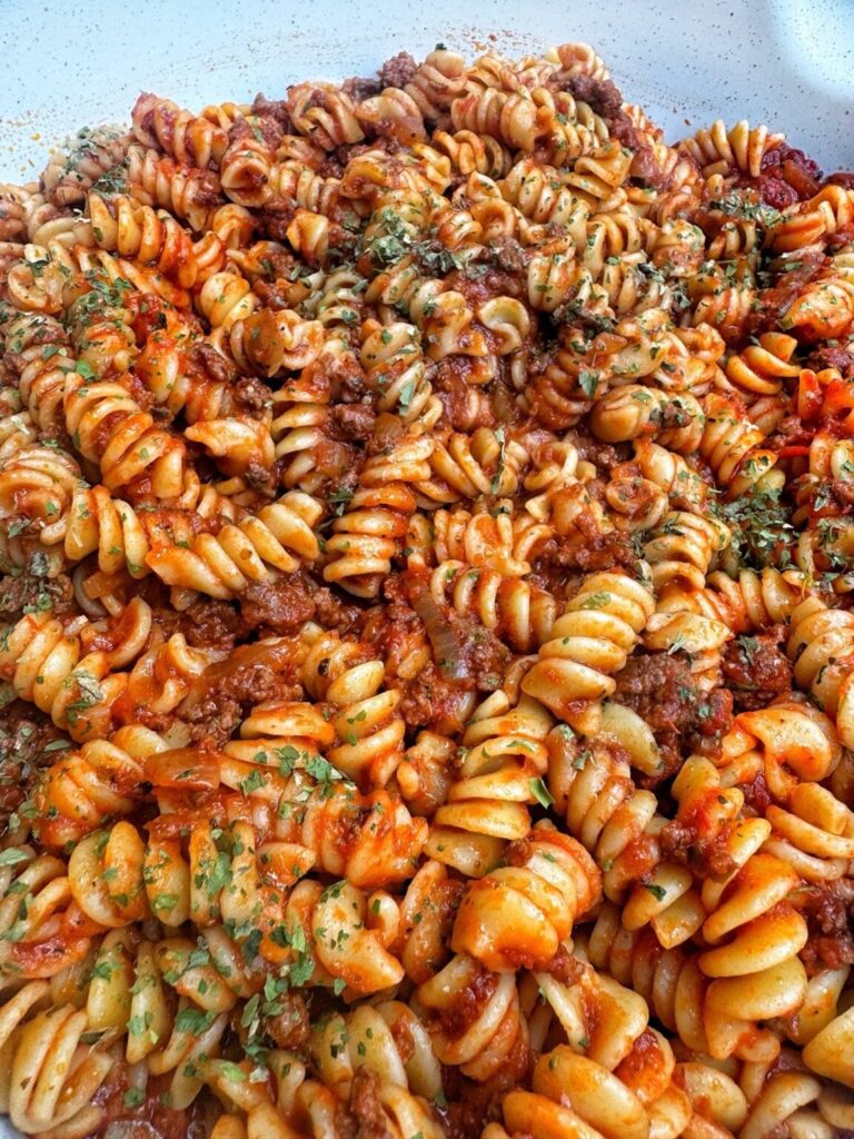 Pan of rotini corkscrew pasta and meat sauce with green herbs