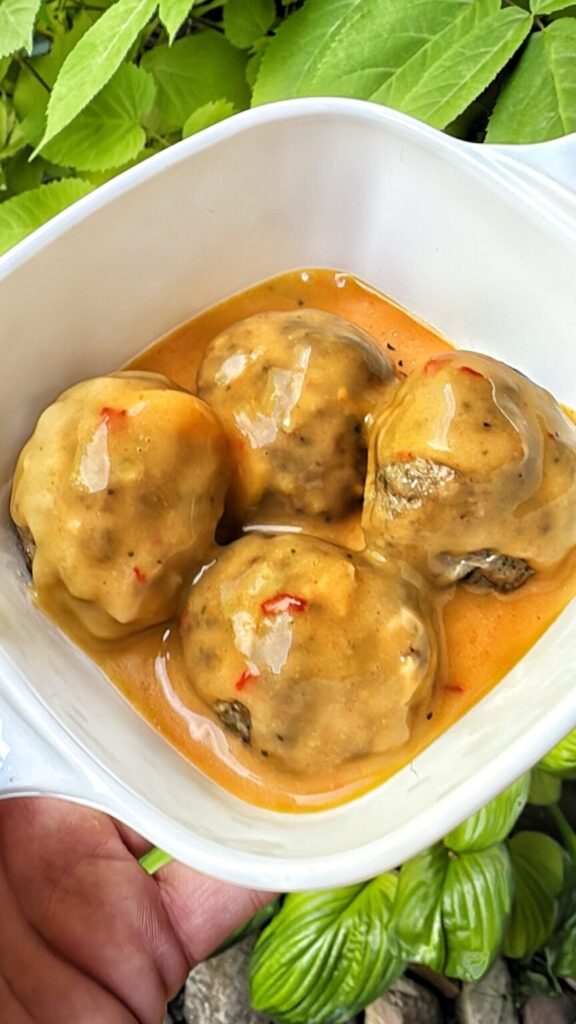 a plate of four meatballs covered in a spicy cheese sauce