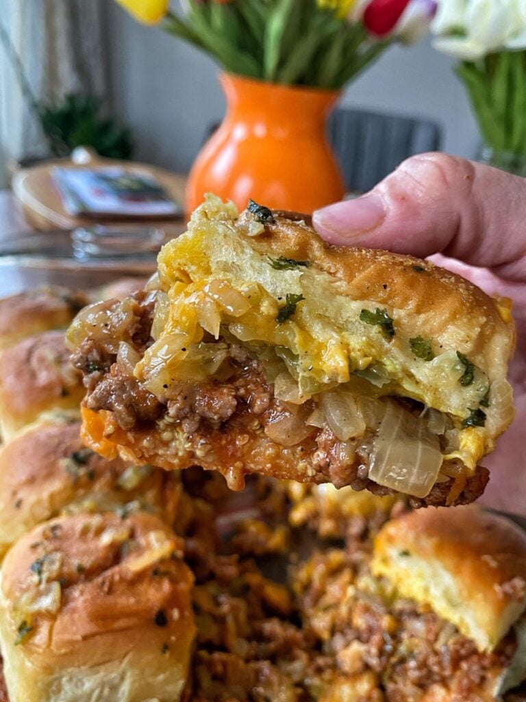Sloppy joe sliders held up by a hand and some onion