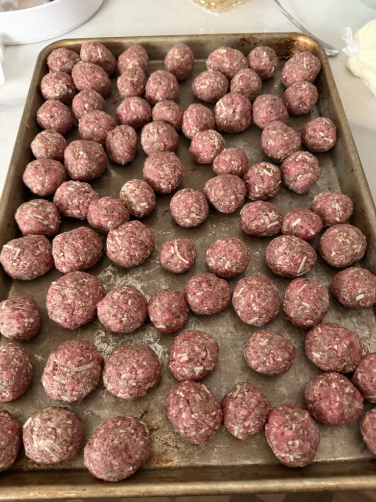 Small uncooked Parmesan beef meatballs arranged on a rimmed baking sheet.
